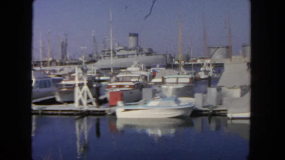 1962 San Diego marina scene with docked boats, covered craft, masts, and a passenger liner beyond the slips.