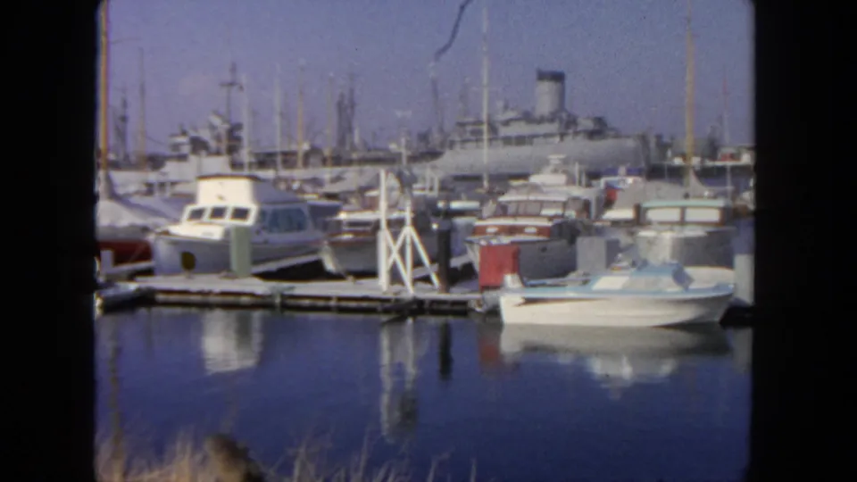 1962 San Diego marina view with docked pleasure boats, sailboat masts, calm blue water reflections, and a larger ship-like vessel beyond.