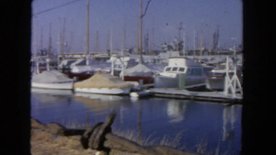 1962 San Diego marina frame with covered and uncovered boats moored beside docks in soft 8mm color.