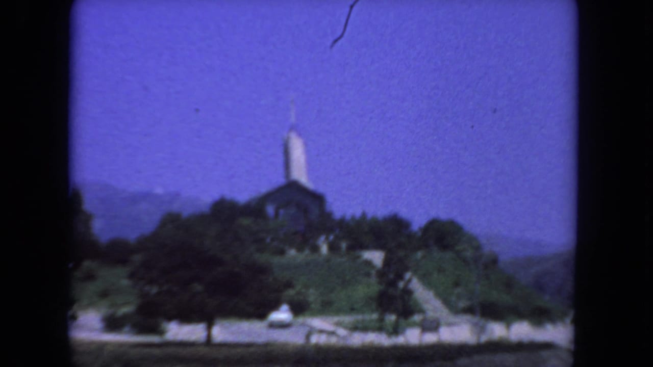 1962 San Diego driving-view frame with a church and steeple on a landscaped hill under a deep blue sky.