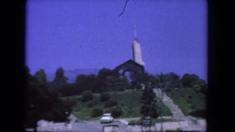 A 1962 San Diego frame shows a church on a green hill, a pale car below, trees, and a walkway or steps up the slope.