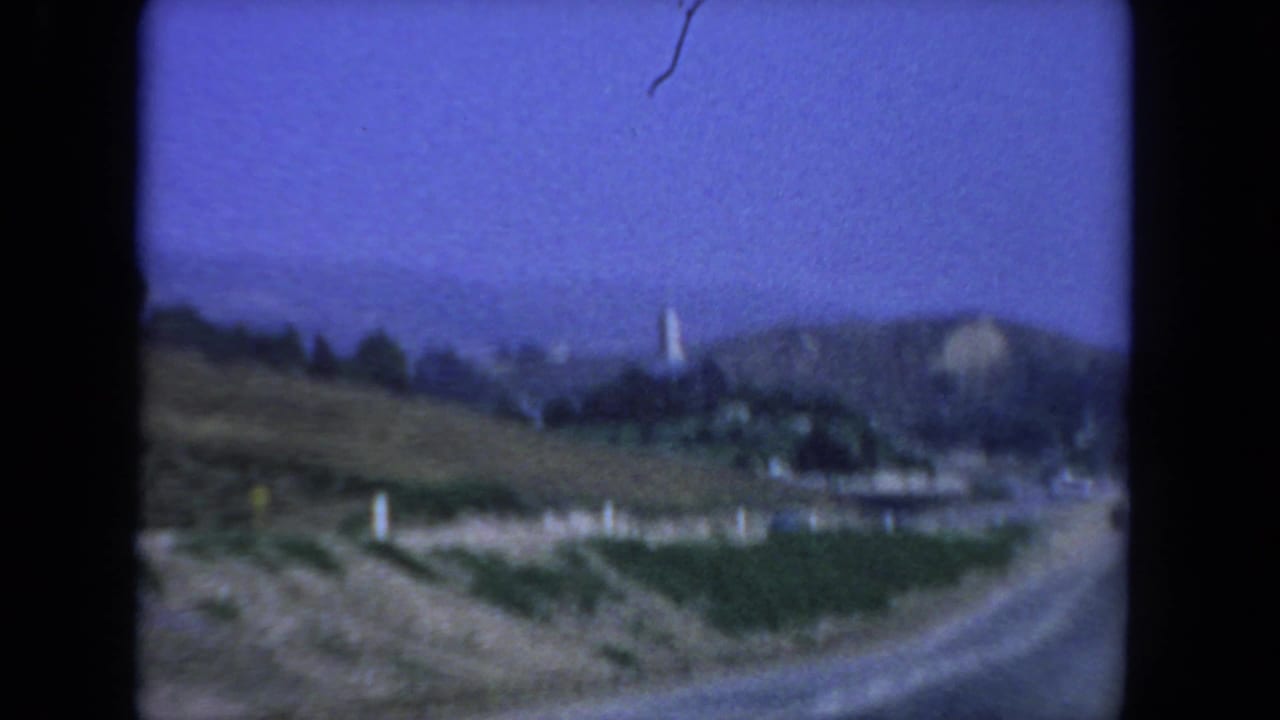 Curving road below scrubby hills with a distant tower-like structure on a ridge.