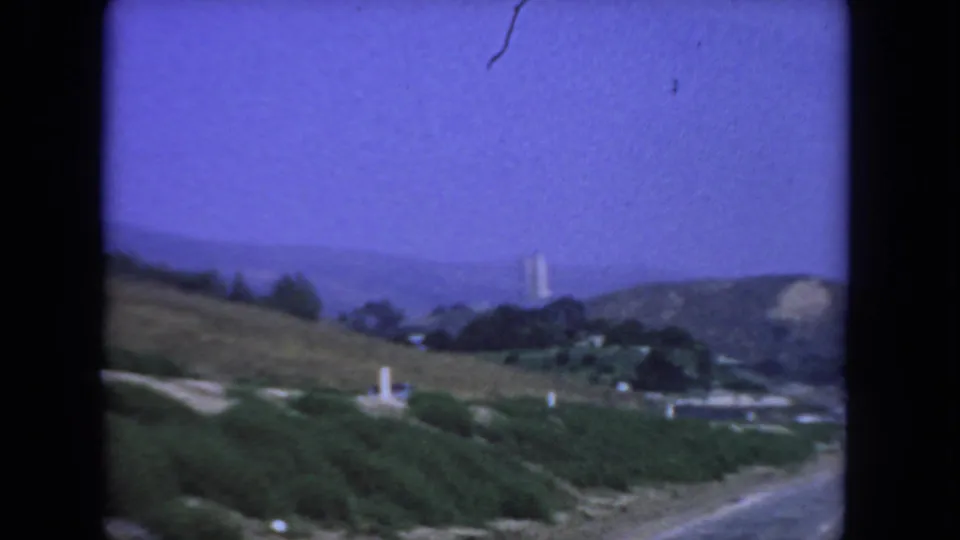 1962 San Diego home-movie frame with foreground brush, rolling hills, a road edge, and distant ridges softened by 8mm color shift.