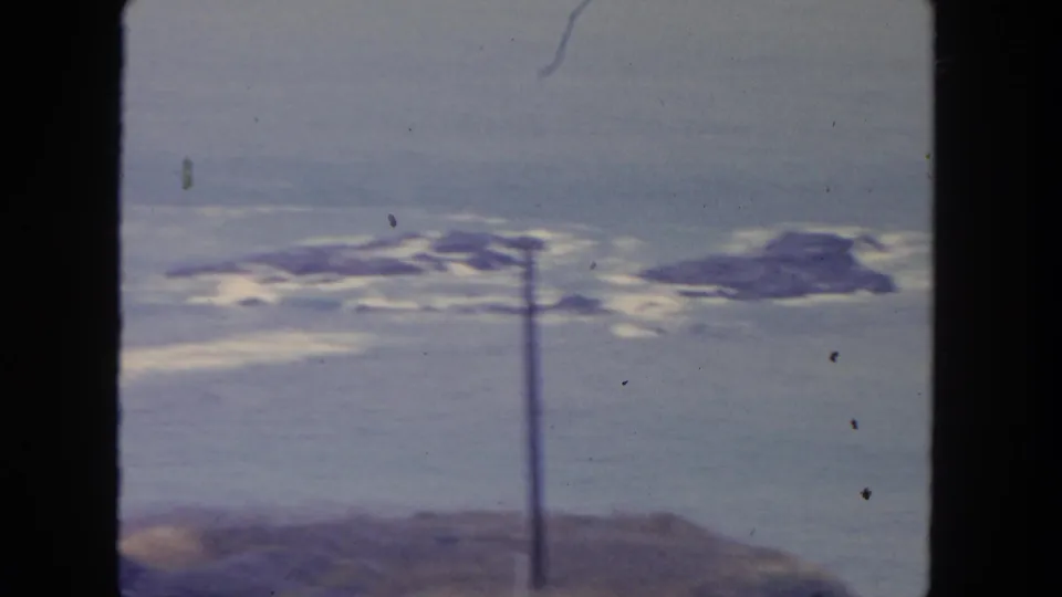1962 San Diego coastal view from a roadside position, showing rocky surf, muted sky, and a utility pole crossing the frame.