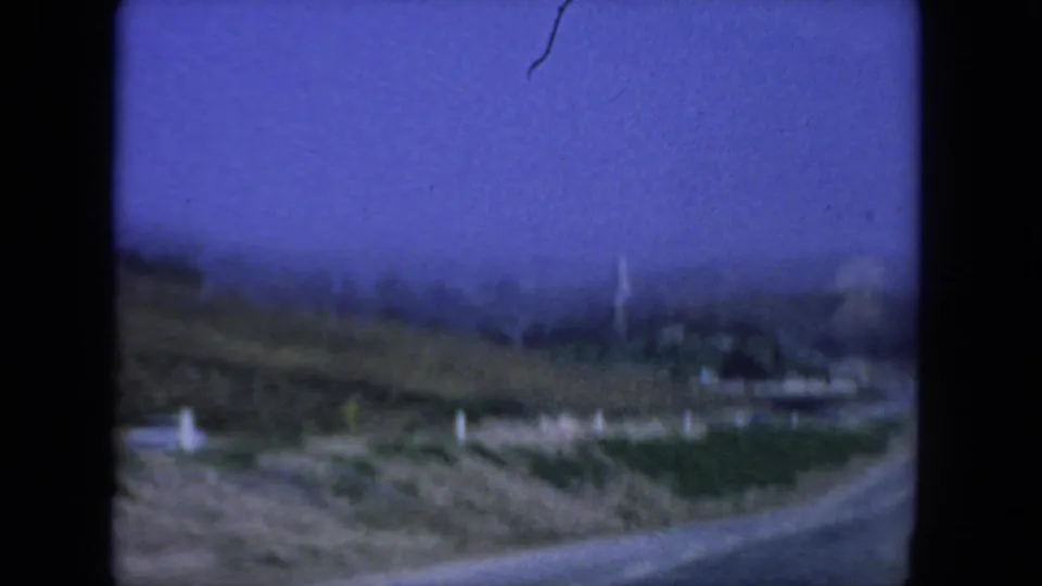 Soft, blue-toned 8mm frame of roadside terrain with distant ocean and sky near the San Diego coast.