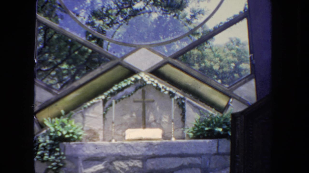 1962 San Diego 8mm frame showing a small stone chapel altar framed by stained glass, plants, and a cross.