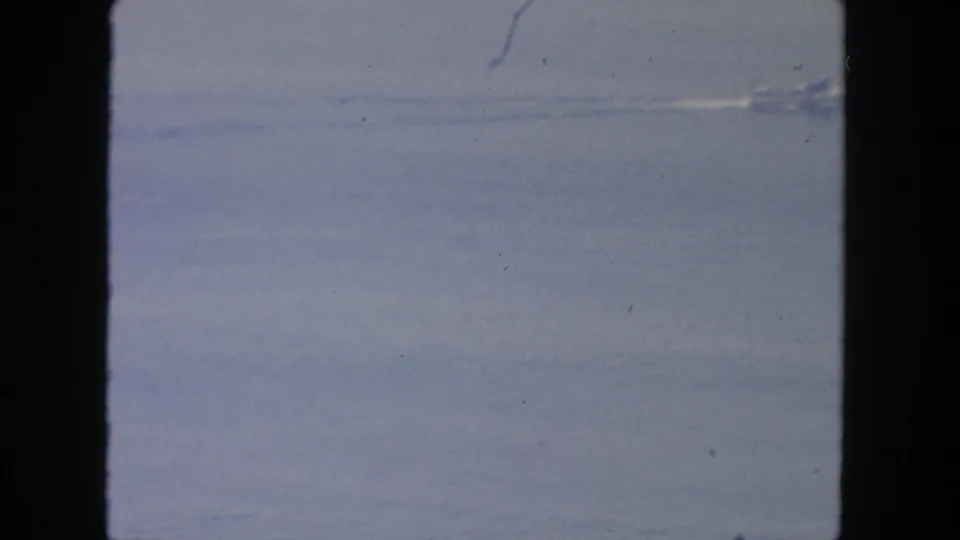 1962 San Diego coastal frame with a small distant boat moving across calm blue water beneath a hazy sky.