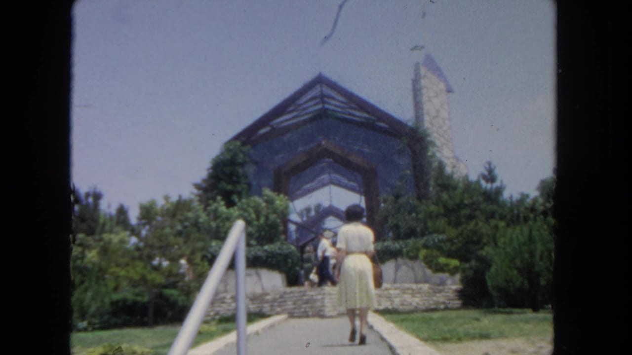 The woman continues toward the stone steps while several visitors stand near the entrance of the San Diego building exterior.