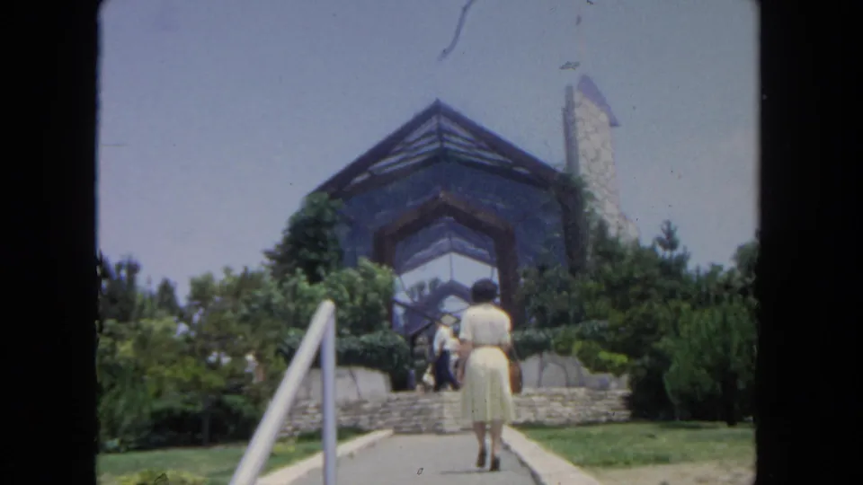 The woman continues toward the stone steps while several visitors stand near the entrance of the San Diego building exterior.