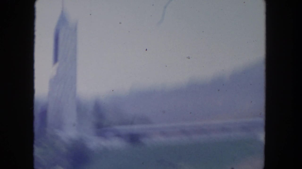 Soft 8mm view of a pale tower rising beyond a low roofline and trees in the San Diego-area footage.