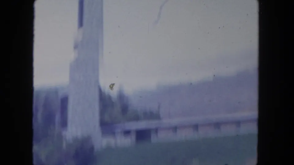 Handheld 1962 San Diego frame with a blurred stone tower, low building, trees, and dark foreground movement.