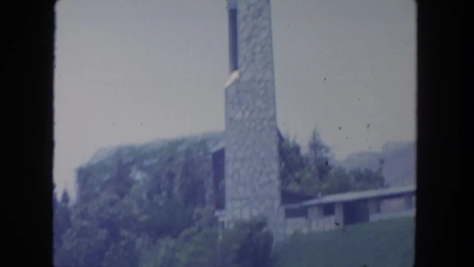 1962 San Diego 8mm frame showing a stone church-like tower near trees, hillside, and a low roofline.