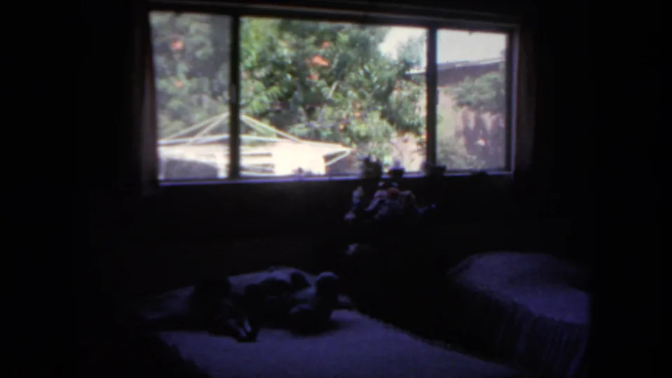 1962 San Diego interior frame showing a dark bedroom with twin beds and a sunlit window view of trees outside.