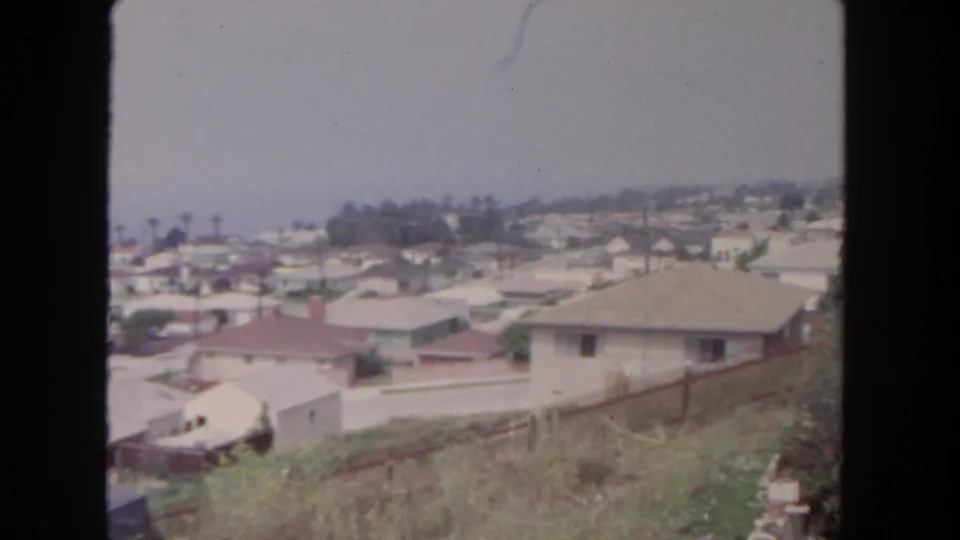 1962 San Diego view across a suburban neighborhood, with rooftops, palms, distant homes, and soft 8mm frame edges.