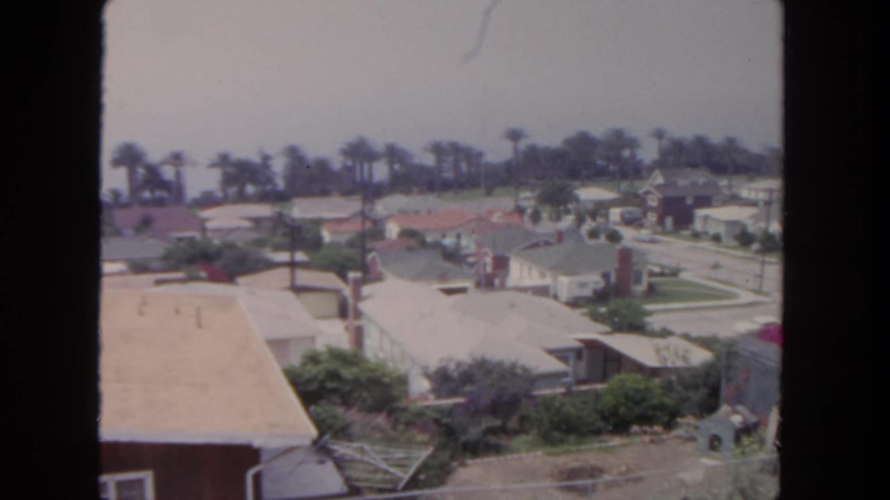 Similar elevated neighborhood view with houses, rooftops, palms, streets, and lawns.