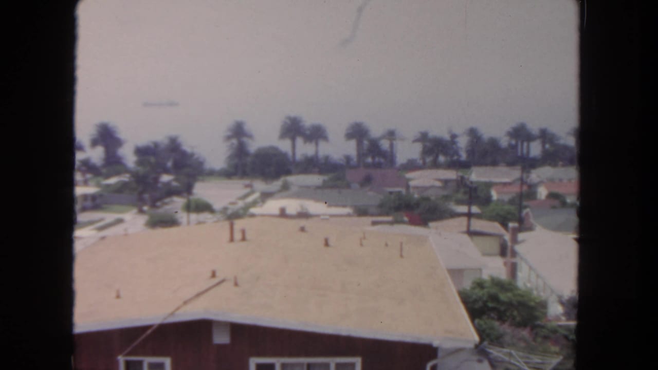 1962 San Diego frame showing rooftops, palms, utility poles, and quiet single-story homes from an elevated angle.