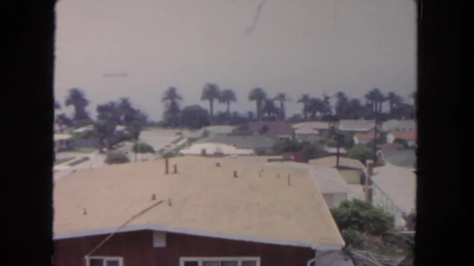 1962 San Diego frame showing rooftops, palms, utility poles, and quiet single-story homes from an elevated angle.