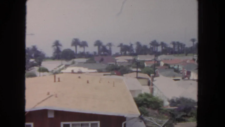 1962 San Diego home-movie view across a tan roof toward low houses, palms, gardens, and a bright hazy sky.