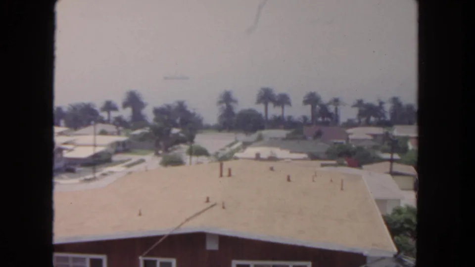1962 San Diego residential panorama ending on a foreground roof, palm-lined homes, quiet streets, and a soft distant horizon.
