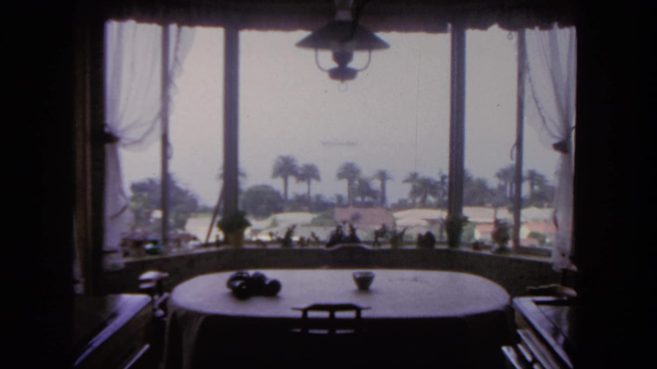 1962 San Diego home-movie view from a dining room table through a bay window toward palms, hazy water, and a distant ship.