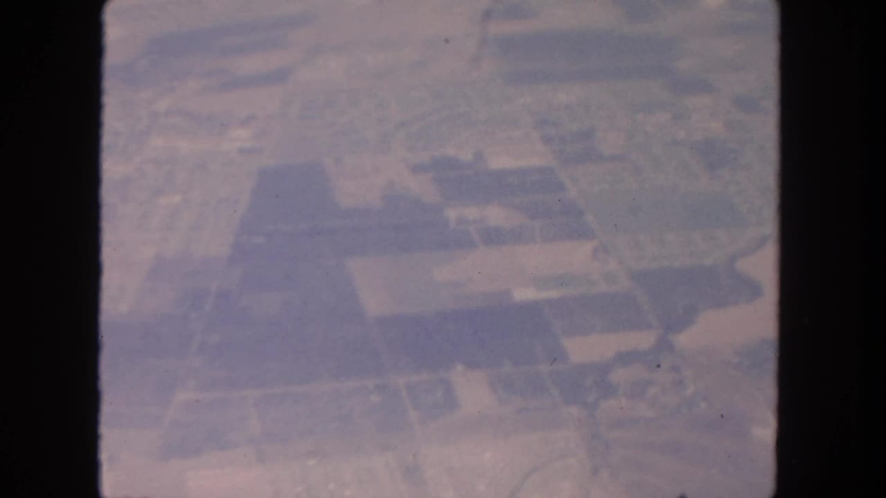 Hazy aerial view of divided farmland and roads through an 8mm film frame.