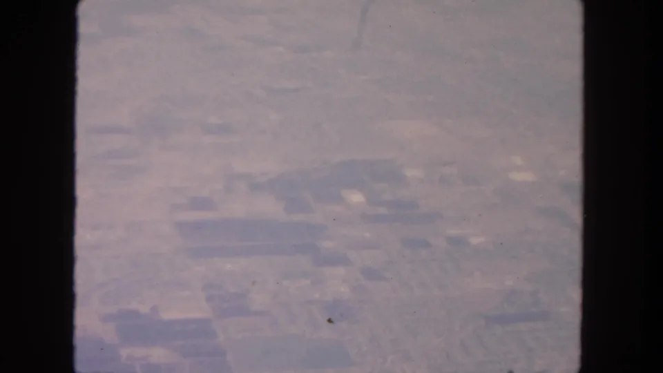 Faded 8mm aerial frame showing farmland, roads, and small building clusters in the San Diego-area travel footage.