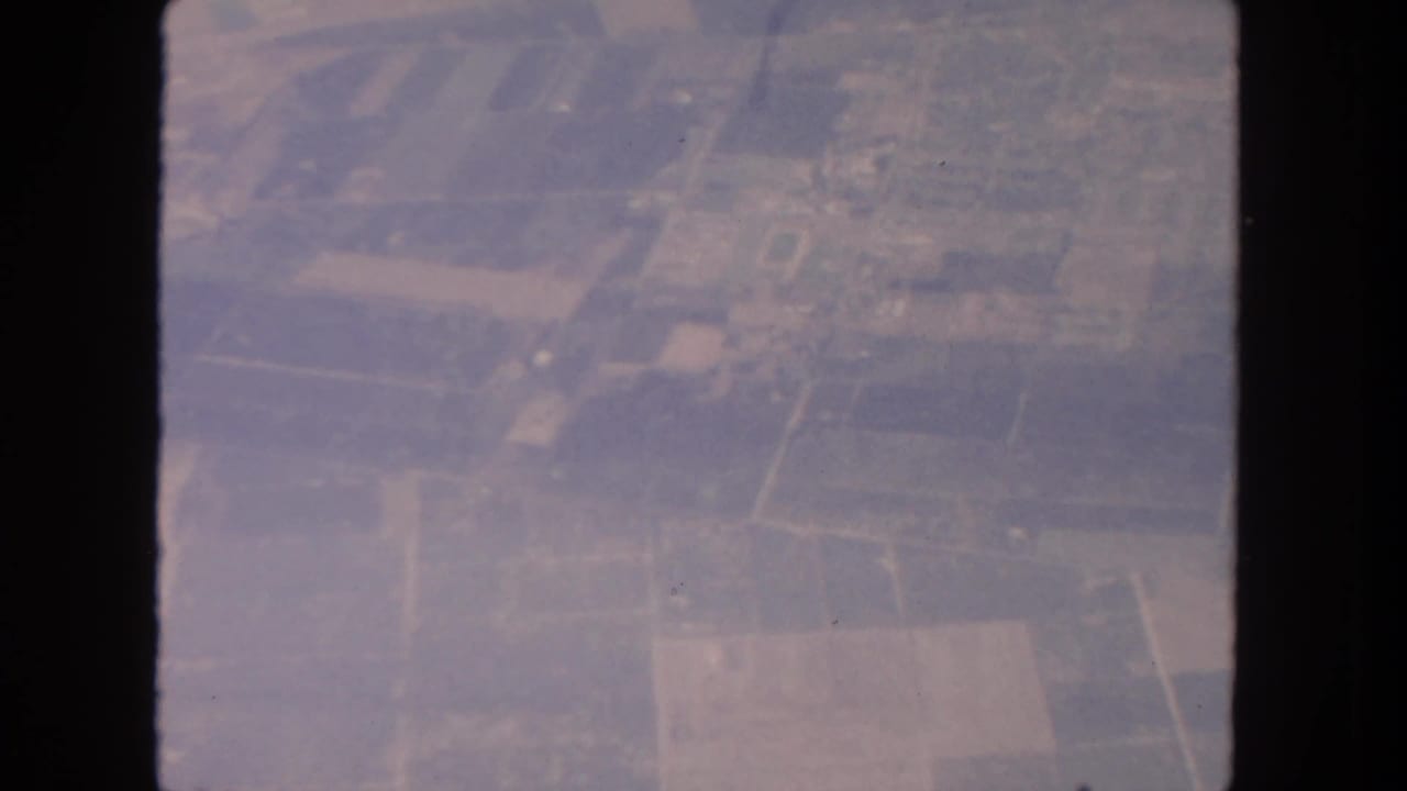 Aerial 8mm frame showing San Diego-area farmland, roads, and scattered structures from above in 1962.