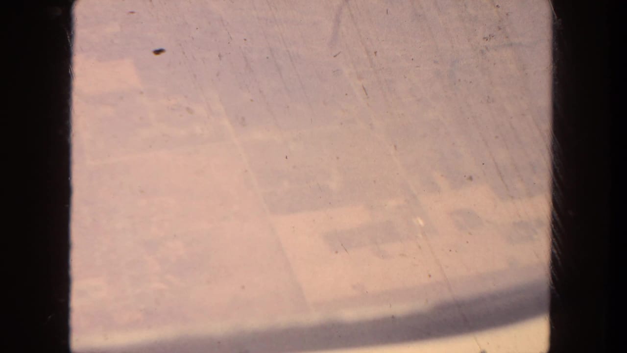 1962 San Diego aerial 8mm frame showing hazy farmland below through dark aircraft-window or film-gate shadows.