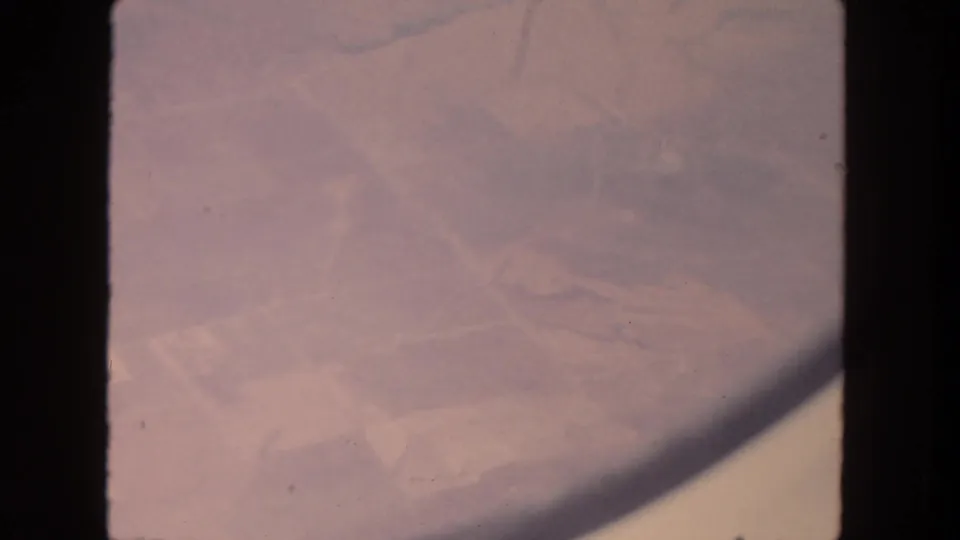 Faded 1962 San Diego aerial frame with farmland below and a curved dark shadow crossing the lower right of the 8mm scan.