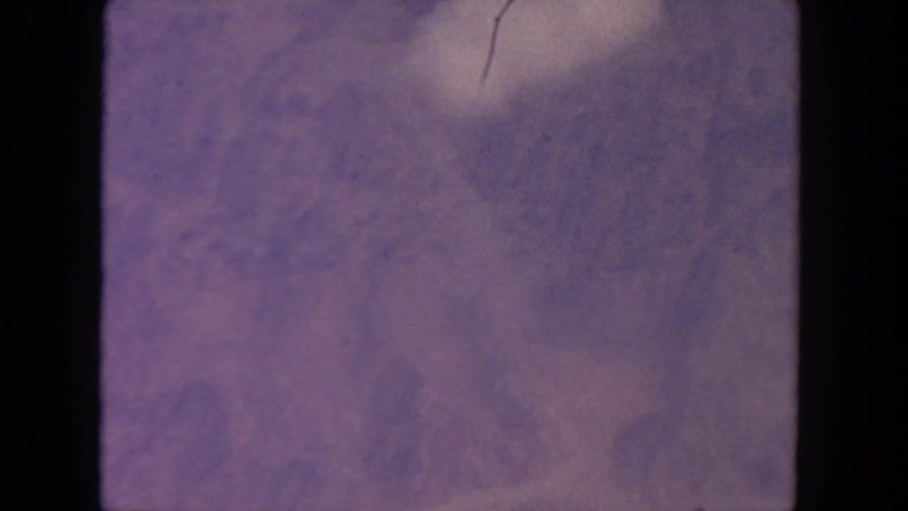 Purple-tinted hazy clouds fill an 8mm film frame with dark rounded borders.