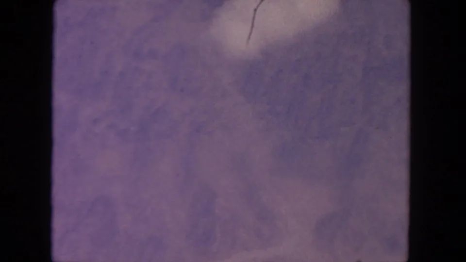 1962 8mm home-movie frame from the San Diego metadata set showing hazy lavender clouds with film grain, scratches, and rounded frame edges.