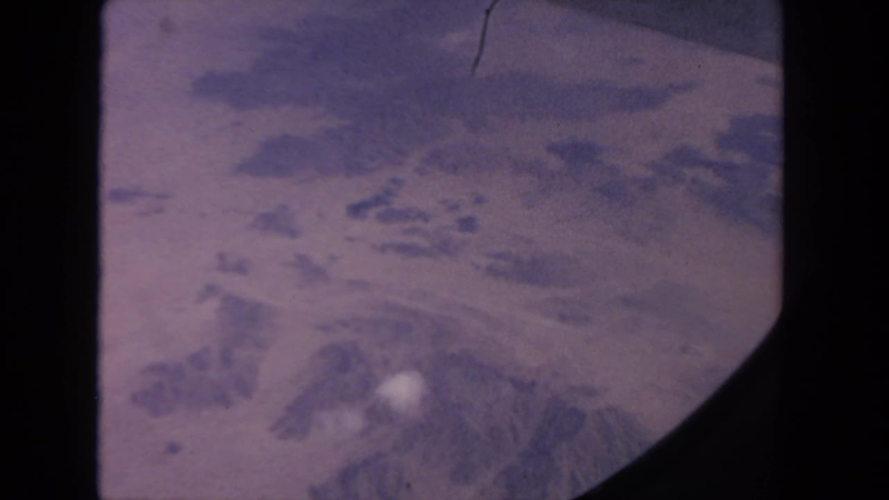 Snow-dusted mountain terrain seen from above through a dark-edged film frame.