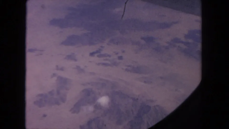 1962 8mm aerial view near San Diego showing hazy snow patches across rugged mountain terrain.