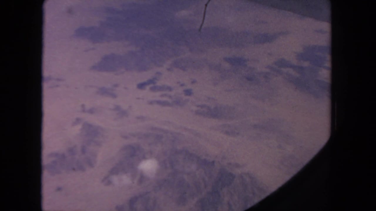 High aerial view of pale mountain slopes with scattered snow and dark film borders.