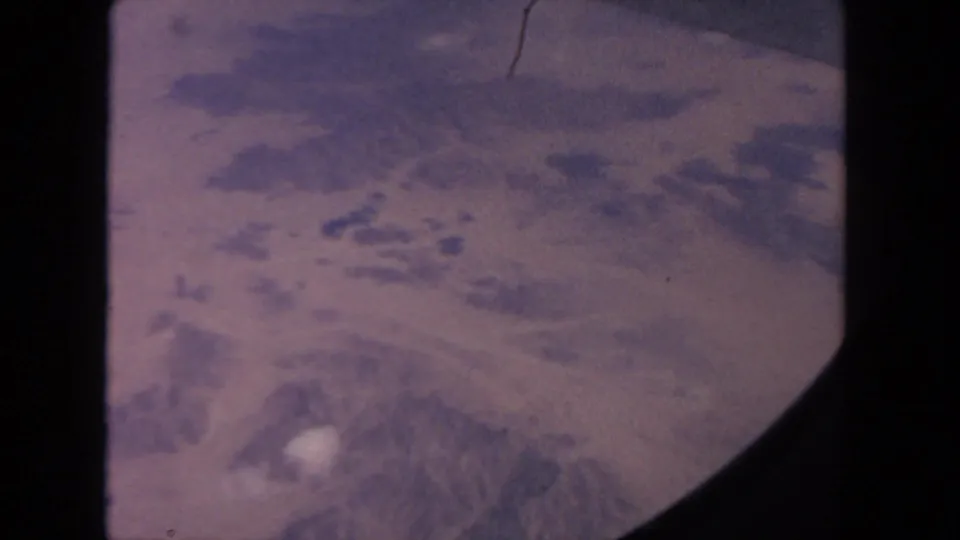 Vintage 8mm aerial frame showing rugged, snow-marked terrain in the San Diego area, with visible film-frame curvature.