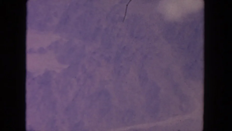 1962 home-movie aerial view near San Diego with muted snowy mountain forms and visible 8mm grain and discoloration.
