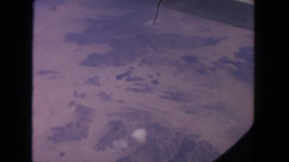 End frame of a 1962 8mm passenger-window aerial view, with hazy terrain and rounded window framing.