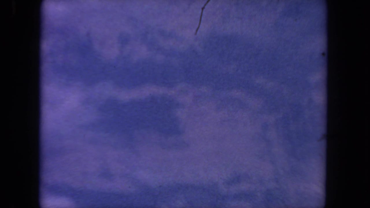 Dark aircraft-window framing around a hazy blue-lavender view of clouds or ground below.