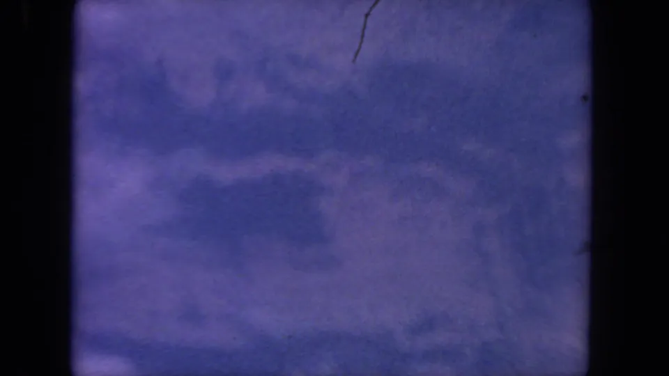 1962 8mm-style airplane-window view from the San Diego-labeled clip, showing a soft blue-lavender aerial scene with film border and scratches.