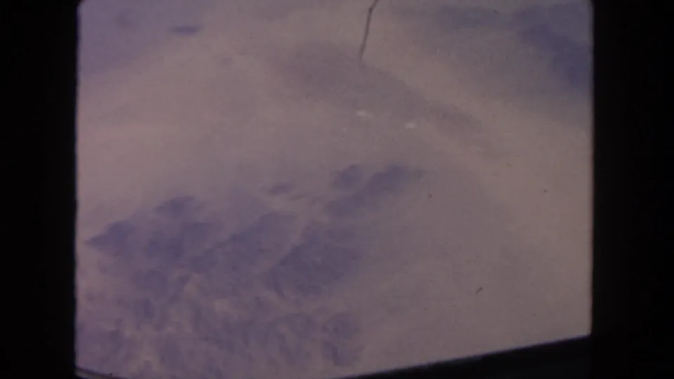 The final frame keeps the airplane-window perspective, with lavender haze, faint ground texture, and visible 8mm film grain and border intrusion.