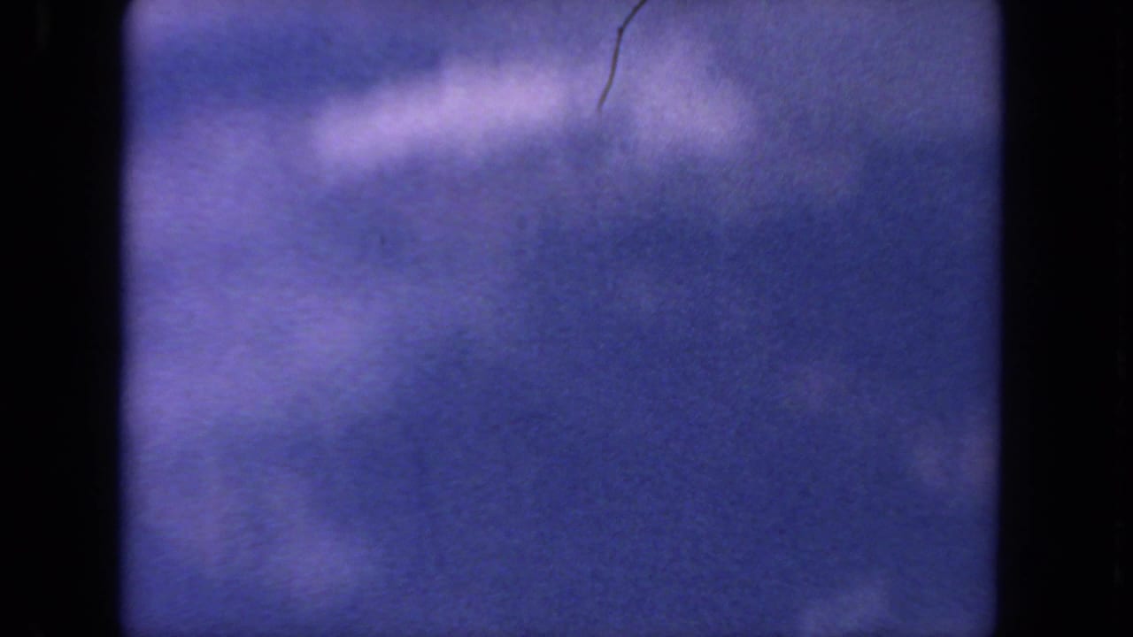 1962 8mm San Diego-area aerial footage with purple-blue sky, diffuse clouds, and heavy dark gate borders.