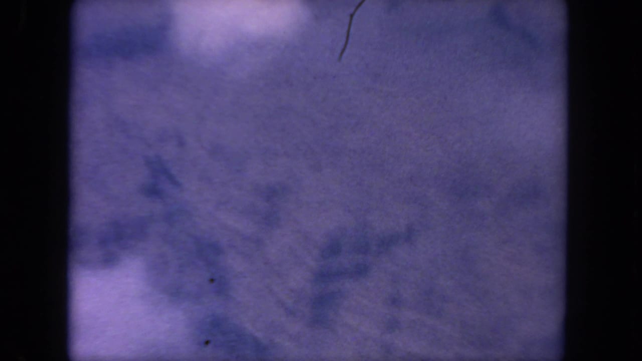 Soft 1962 8mm aerial frame from the San Diego metadata, showing purple haze, pale cloud forms, and visible film wear.