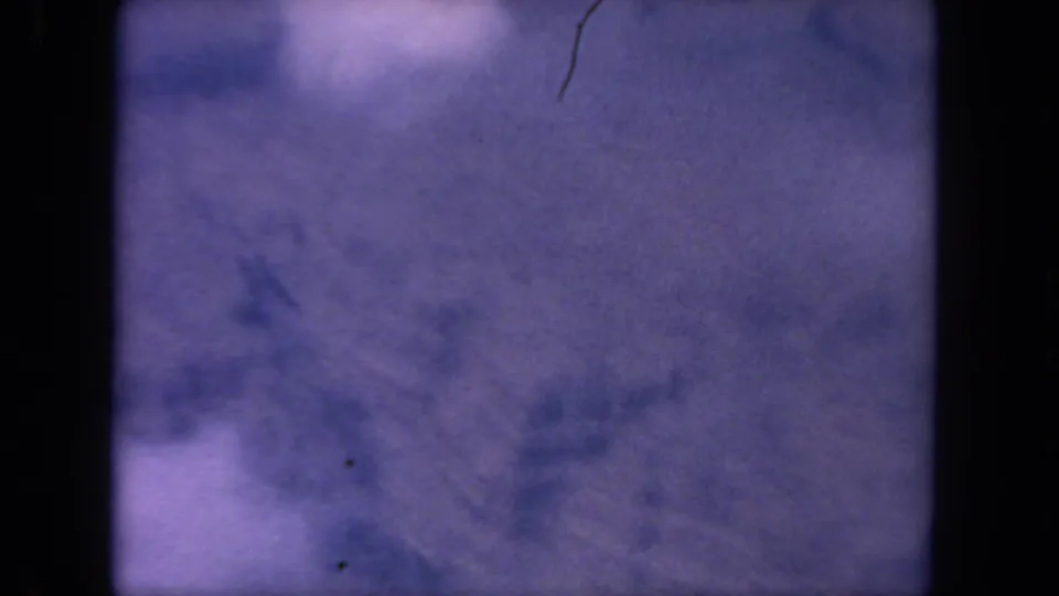 Soft 1962 8mm aerial frame from the San Diego metadata, showing purple haze, pale cloud forms, and visible film wear.