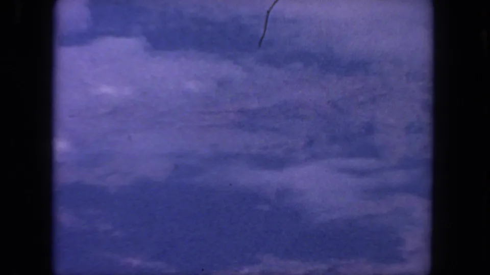 1962 San Diego 8mm frame showing a clouded blue sky, gate edges, grain, and a small visible scratch near the upper area.