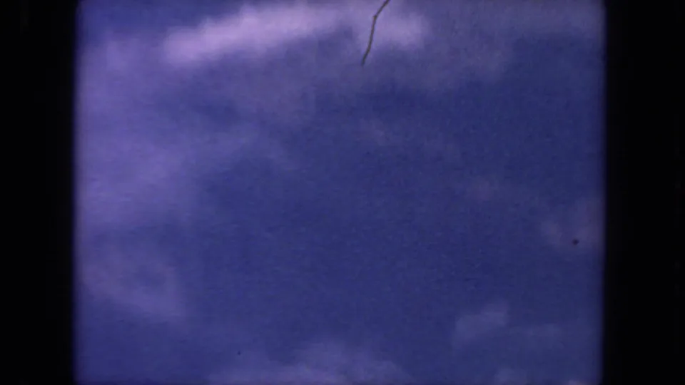 1962 San Diego 8mm frame with open blue sky, faint white clouds, visible grain, dust, and dark gate edges.