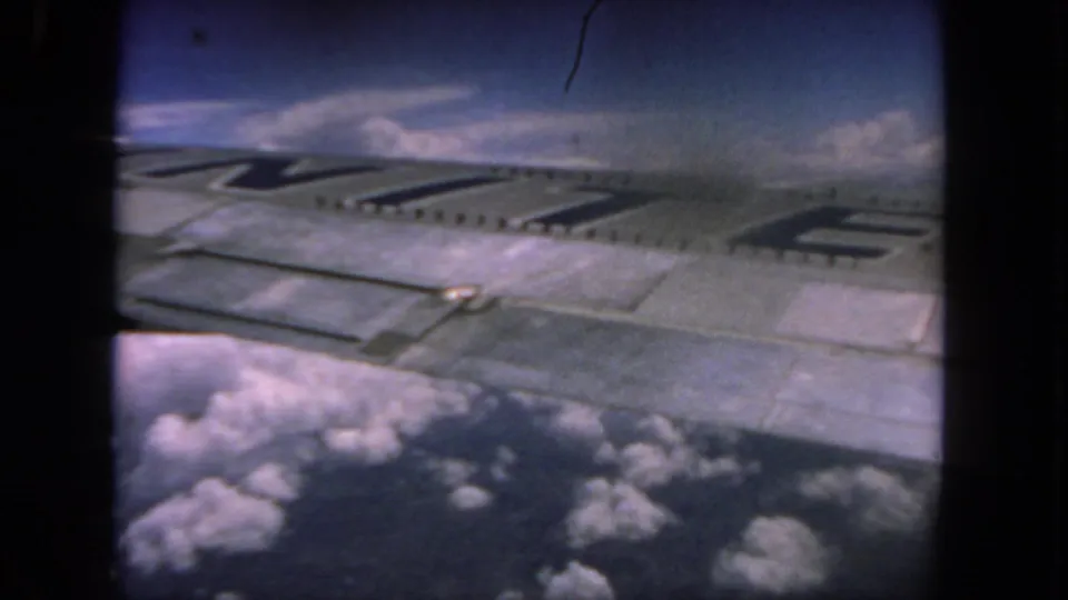 1962 8mm home-movie frame from a flight near San Diego, showing an aircraft wing with dark lettering over cloud tops.