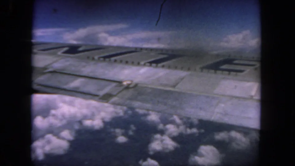 A 1962 airplane-window view shows the wing and partial dark lettering against clouds and a deep blue sky.