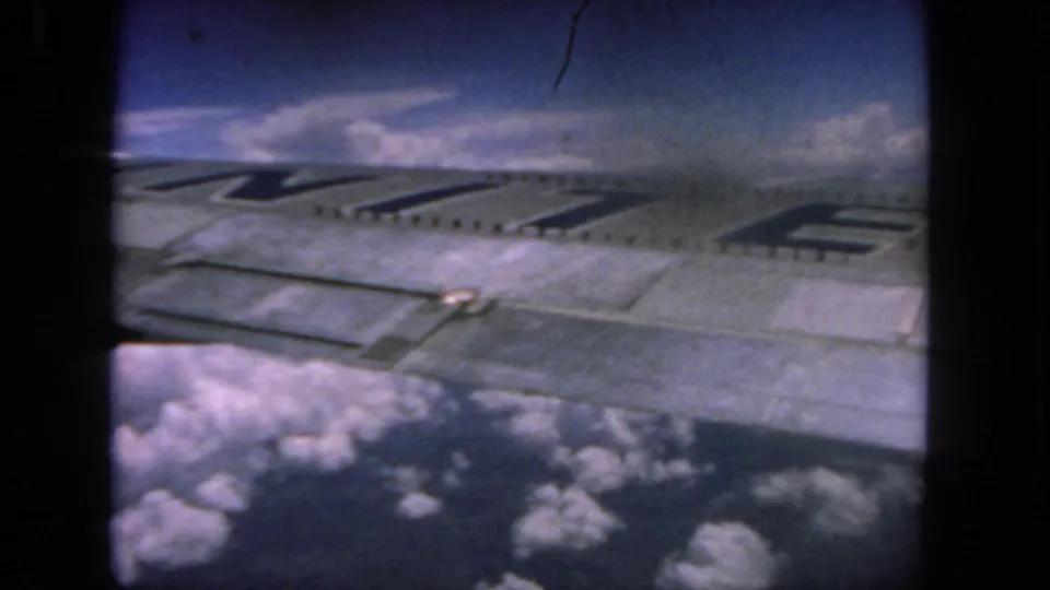 Home-movie footage from 1962 shows a close passenger-window view of an aircraft wing over scattered clouds.