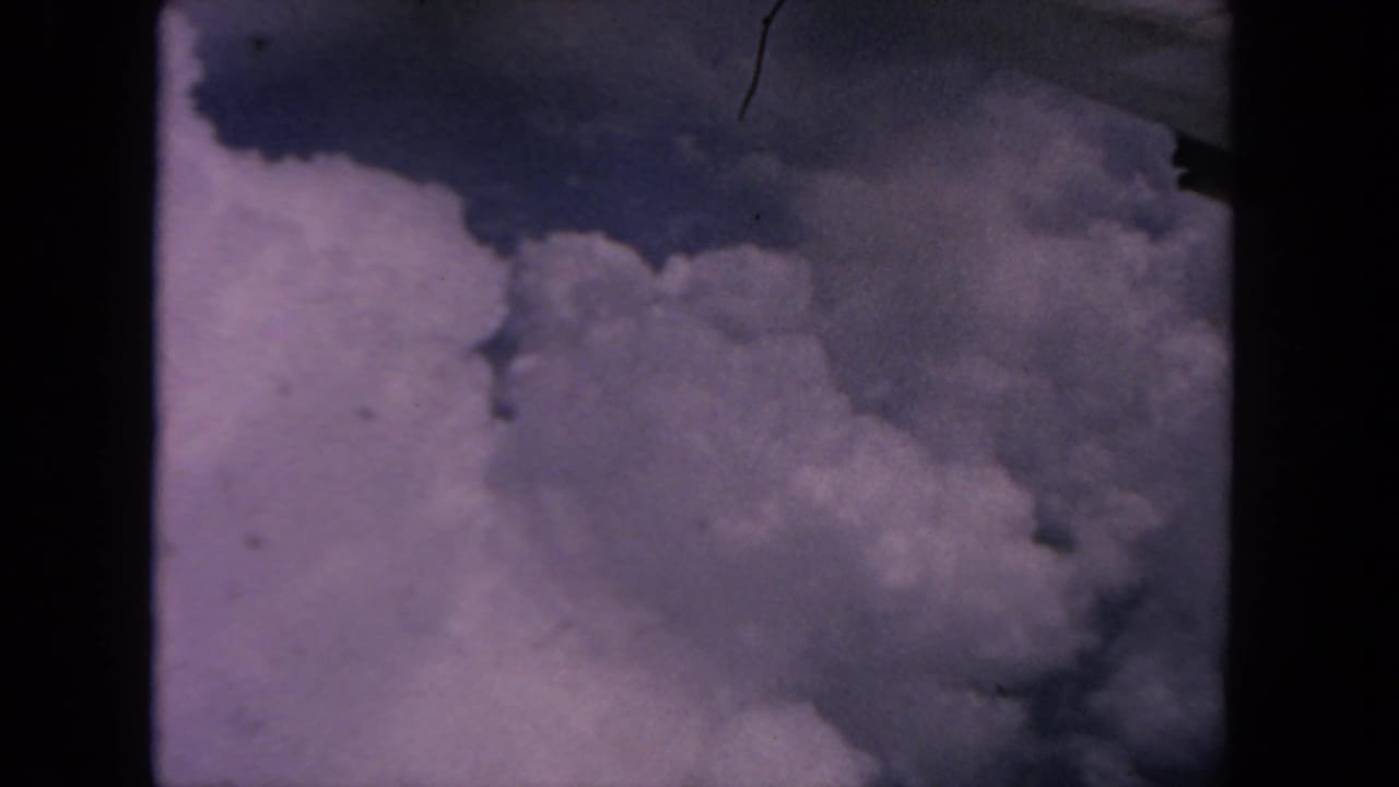 1962 8mm passenger-window view near San Diego showing bright clouds below a partial airplane wing edge.