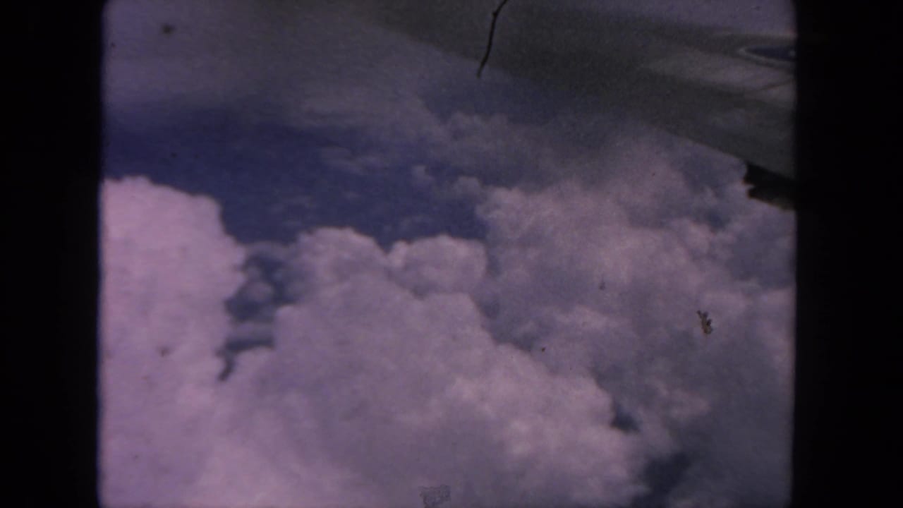 1962 8mm view from an airplane window over cloud tops, with no people or markings visible.